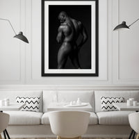 The inside wall of a modern classically styled restaurant with framed artwork hanging on the wall, the art is a black and white fine art photo of a nude black man posterior view from head to mid thigh with one arm bent and chin resting on closed fist.