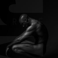 Black and white fine art photo showing a sideview of a nude black man crouching with arms resting on knees and head tilted down.