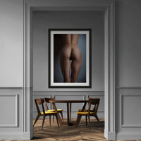 Framed artwork hanging above a diningroom table, the art is a fine art photo of nude woman from back, showing her naked body from her lower back to her upper thighs with the light reflecting off of her shapely buttocks.