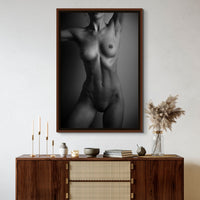 Framed canvas artwork hanging above a brown walnut credenza, the art is a black and white fine art photo of a nude woman standing facing the camera. The photo is cropped to show the model from her chin to her mid thigh.