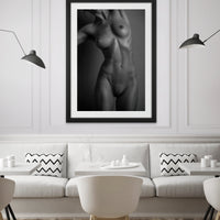 The inside wall of a modern classically styled restaurant with framed artwork hanging on the wall, the art is a black and white photo of a nude woman standing facing the camera. The photo is cropped to show the model from her chin to her mid thigh.