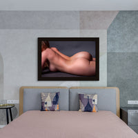 Portrait hanging above a bed of close up of a nude woman portrait. The woman is lying on her side, the image is cropped to show from her shoulders to the top of her thighs.