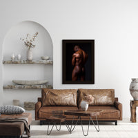 Fine art photo hanging above a brown leather sofa in a modern livingroom of a nude black man posterior view from head to mid thigh with arms crossed, looking downwards.