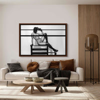 Framed fine art photo hanging above a sofa in a stylish livingroom of a nude woman wearing a black balaclava and black leather gloves and thigh high boots lounging on a bench with one arm bent and resting her handgun against her head in a seductive way.