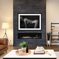 Framed fine art photo hanging above a fireplace in a stylish casual livingroom showing a black and white image of woman on hands and knees, with her long hair partially hiding her face. The eye is drawn to the natural curve in her lower back.