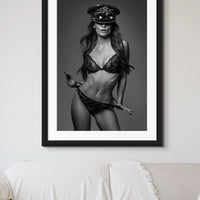 Black framed artwork hanging above a sofa in a neutral casual livingroom, the art is a black and white portrait of a gorgeous woman wearing a lace bra and panties with a steampunk style captain's hat and round goggles on her head facing the camera with her thumbs hooked in her panties.