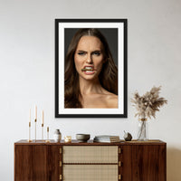 Framed artwork hanging above a brown walnut credenza, the art is a close up portrait of a beautiful woman holding a bullet between her teeth with her brow furrowed.