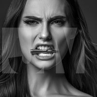 Close up black and white portrait of a beautiful woman holding a bullet between her teeth with her brow furrowed.