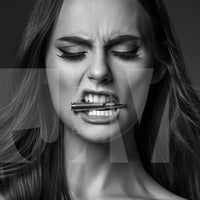 Close up black and white portrait of a beautiful woman holding a bullet between her teeth with her brow furrowed.