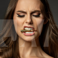 Close up portrait of a beautiful woman holding a bullet between her teeth with her brow furrowed.