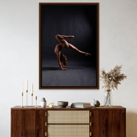 Framed canvas artwork on canvas hanging above a brown walnut credenza, the art is a photo of a sideview of a nude woman in a handstand pose, balance with one leg pointed straight back behind the woman and the other knee bent directly above the woman.