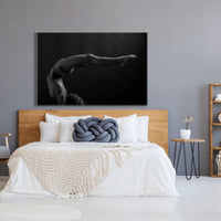 Canvas artwork hanging above a light coloured wood headboard in a bedroom with natural and blue tones, the art is a black and white photograph of a sideview of a nude woman in a handstand pose with back arched in a sweeping curve with legs stretching out behind her.