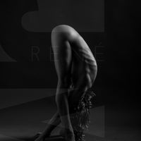 Black and white fine art photography of a side body view of a lean beautiful nude woman hinged at hips with hands reaching through legs and placed on the floor.