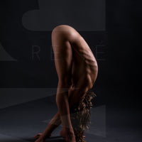 Fine art photography of lean beautiful nude woman hinged at hips and folded in half with hands reaching through legs and placed on the floor.