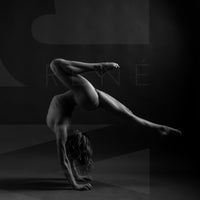 Black and white photo showing a sideview of a nude woman in a handstand pose, balance with one leg pointed straight back behind the woman and the other knee bent directly above the woman.