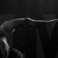 Black and white photo showing a sideview of a nude woman in a handstand pose with back arched in a sweeping curve with legs stretching out behind her.