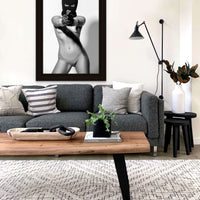 Framed artwork hanging above a sofa in a modern livingroom, the artwork is a black and white photo of a nude woman wearing a black balaclava and black gloves holding a handgun, looking and pointing the gun directly at the camera.