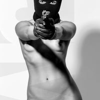 Black and white photo of a nude woman wearing a black balaclava and black gloves holding a handgun, looking and pointing the gun directly at the camera.