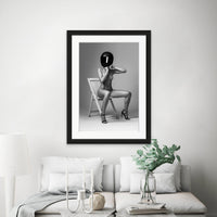 Framed artwork hanging above sofa, the artwork is a black and white photo of nude woman wearing a black motorcyle helmet and black high heels sitting on chair adjusting helmet strap.