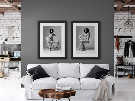 A pair of stylish portraits of a nude woman wearing only a motorcycle helmet are hanging above a sofa in a stylish loft apartment