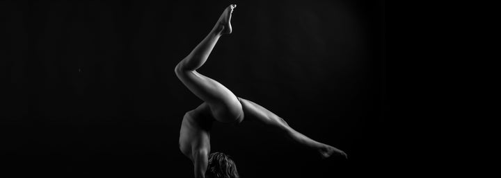 Black and white photo showing a sideview of a nude woman in a handstand pose with arched back and one leg bent with the other straight behind her.