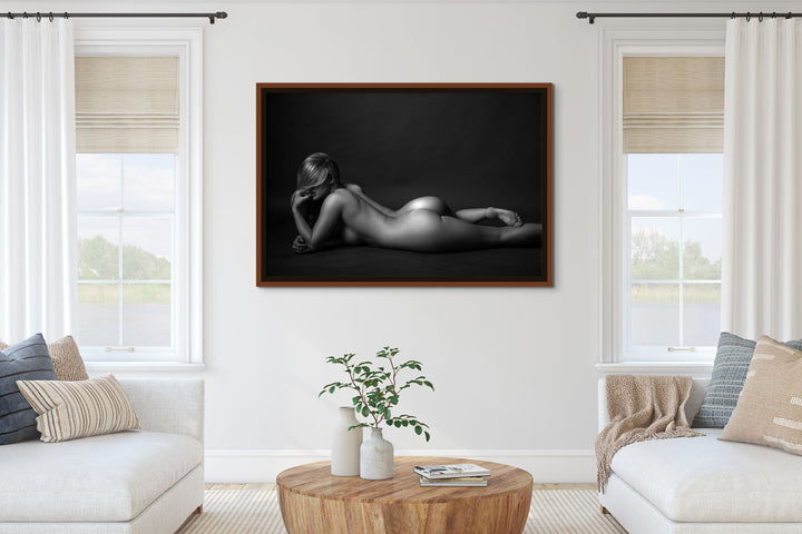 Black and white framed portrait of a nude woman hanging between two windows in a bright neutral living room.
