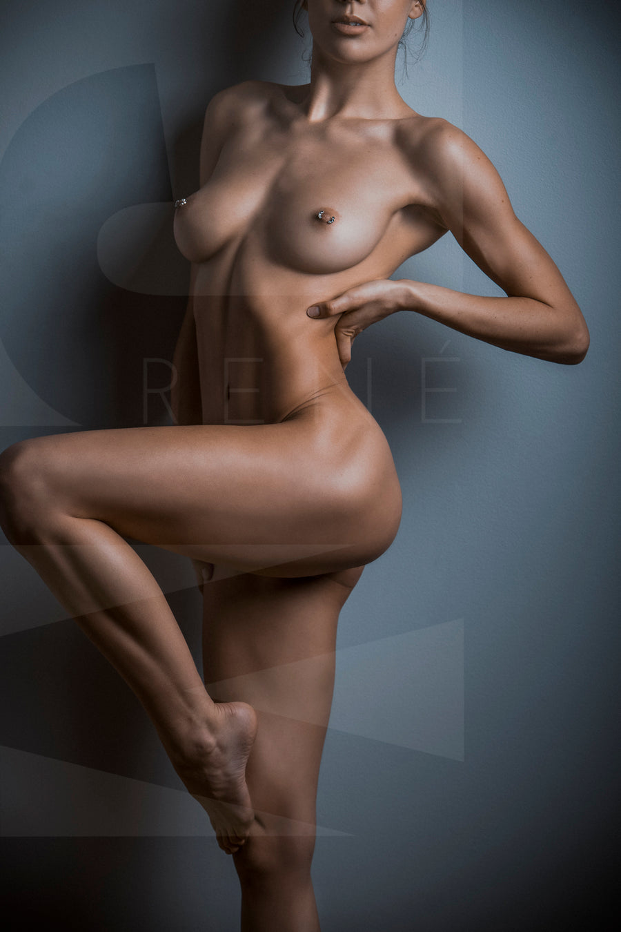 Fine art photo of nude woman from her chin to her knee, showcasing her lines and curves by standing one one leg with the other knee bent so we can see the full length of her leg.