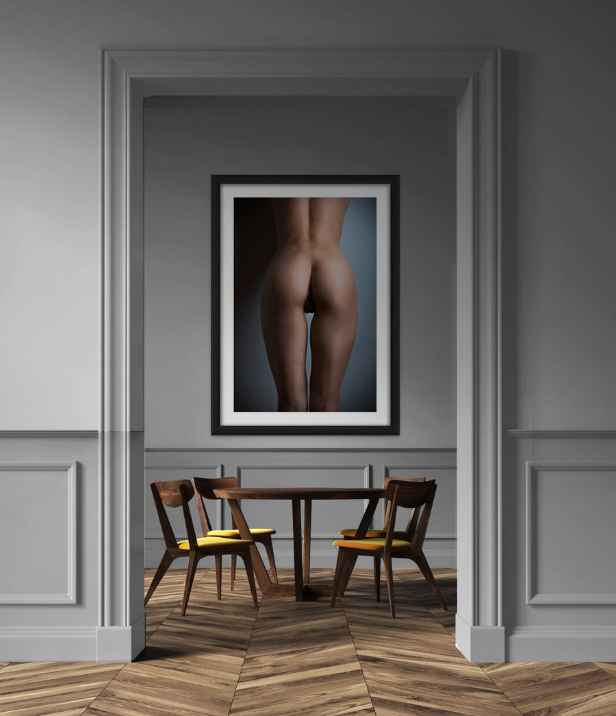 Framed artwork hanging above a diningroom table, the art is a fine art photo of nude woman from back, showing her naked body from her lower back to her upper thighs with the light reflecting off of her shapely buttocks.