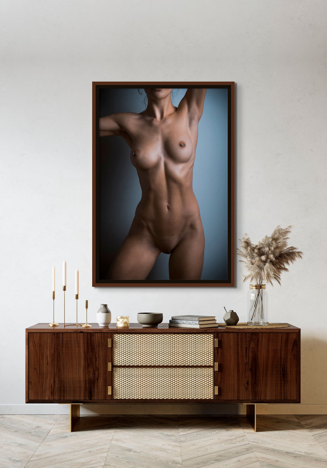Framed canvas artwork hanging above a brown walnut credenza, the art is a fine art photo of a nude woman standing facing the camera. The photo is cropped to show the model from her chin to her mid thigh. 