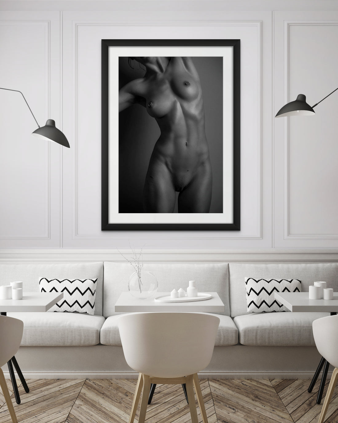 The inside wall of a modern classically styled restaurant with framed artwork hanging on the wall, the art is a black and white photo of a nude woman standing facing the camera. The photo is cropped to show the model from her chin to her mid thigh. 