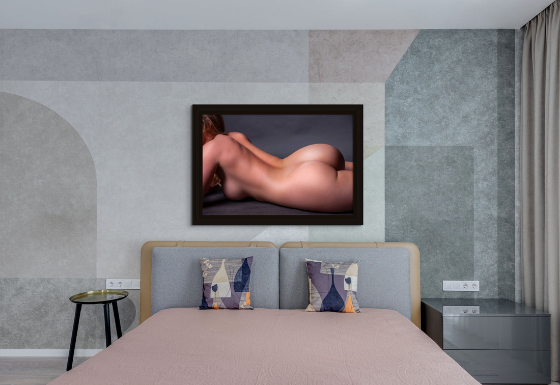 Portrait hanging above a bed of close up of a nude woman portrait. The woman is lying on her side, the image is cropped to show from her shoulders to the top of her thighs.