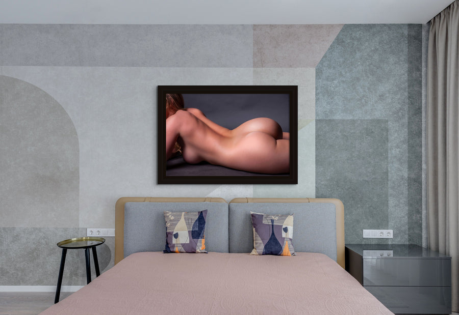 Portrait hanging above a bed of close up of a nude woman portrait. The woman is lying on her side, the image is cropped to show from her shoulders to the top of her thighs.