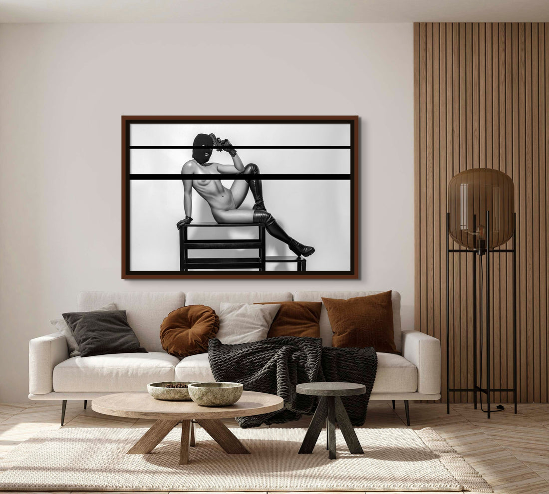 Framed fine art photo hanging above a sofa in a stylish livingroom of a nude woman wearing a black balaclava and black leather gloves and thigh high boots lounging on a bench with one arm bent and resting her handgun against her head in a seductive way.