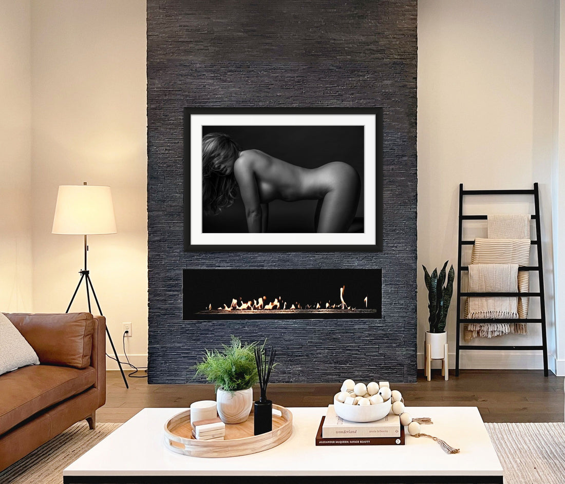 Framed fine art photo hanging above a fireplace in a stylish casual livingroom showing a black and white image of woman on hands and knees, with her long hair partially hiding her face. The eye is drawn to the natural curve in her lower back.