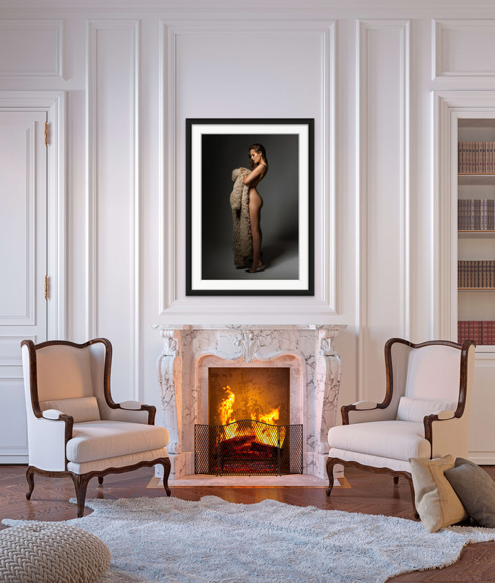 Framed fine art photo hanging above a formal fireplace  shows a sideview of a nude woman wearing high heels looking down at the fur coat she is holding in her arms.