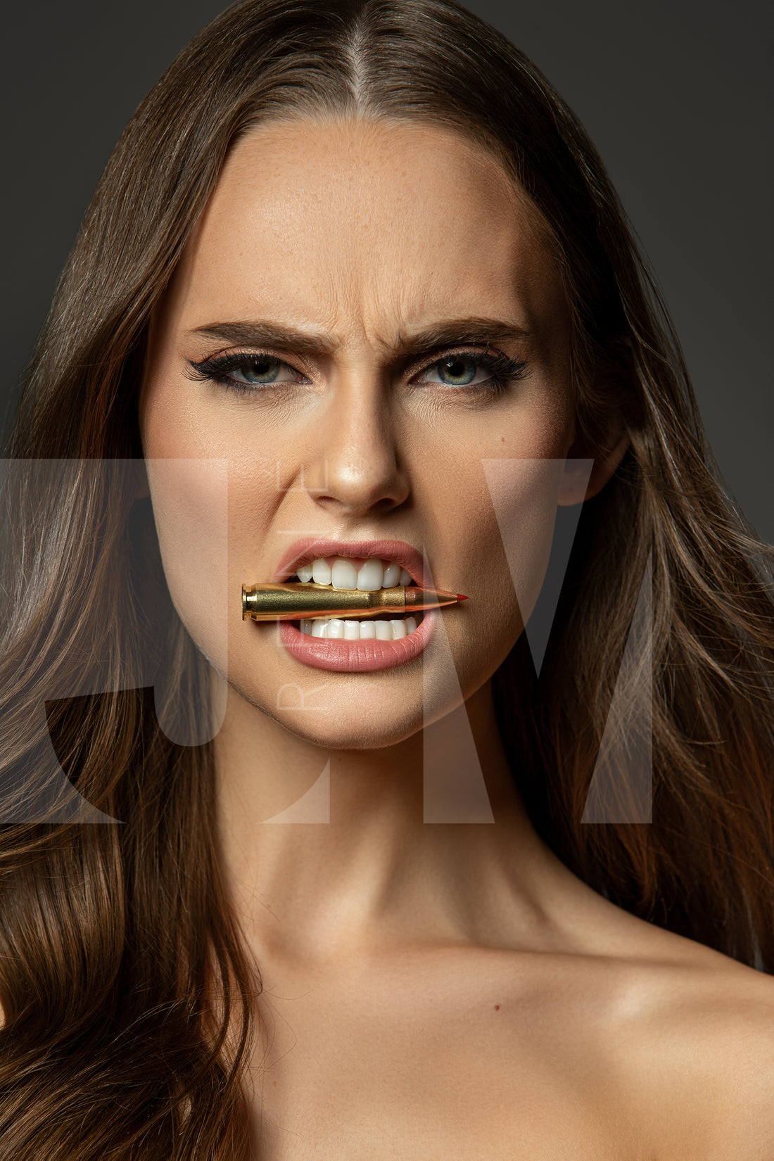 Close up portrait of a beautiful woman holding a bullet between her teeth with her brow furrowed.