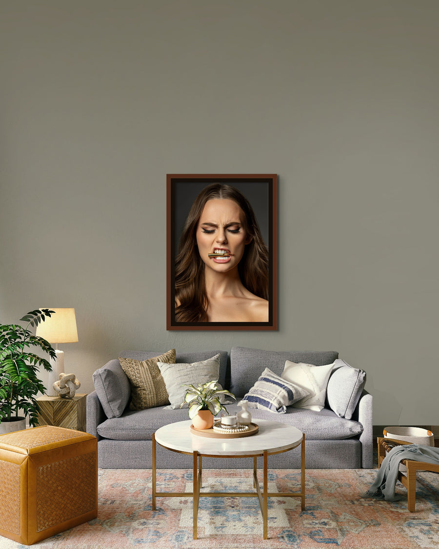 Framed photography artwork hanging above the sofa in a boho-glam style livingroom, the art is a  portrait of a beautiful woman holding a bullet between her teeth with her brow furrowed. 
