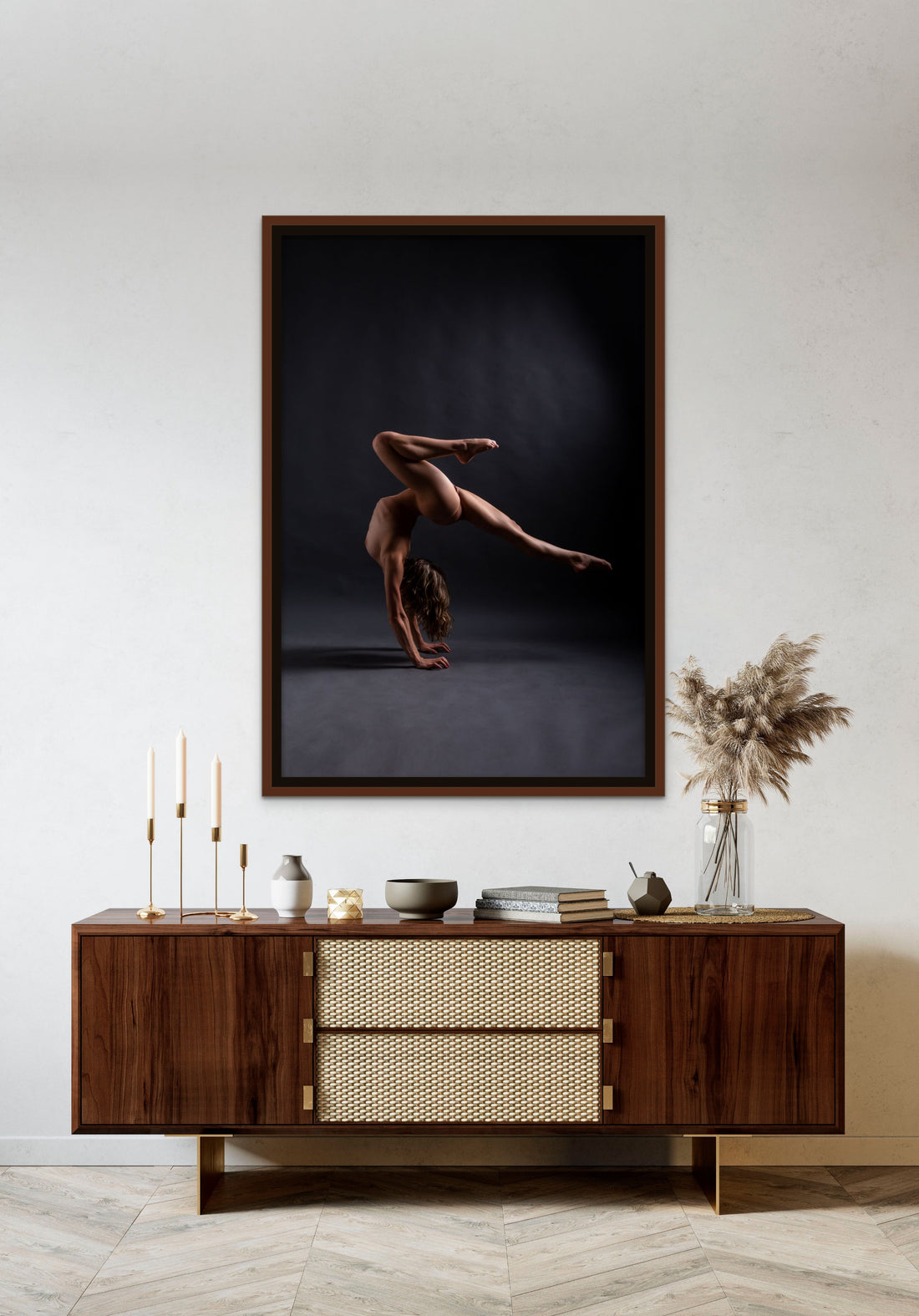 Framed canvas artwork on canvas hanging above a brown walnut credenza, the art is a photo of a sideview of a nude woman in a handstand pose, balance with one leg pointed straight back behind the woman and the other knee bent directly above the woman.