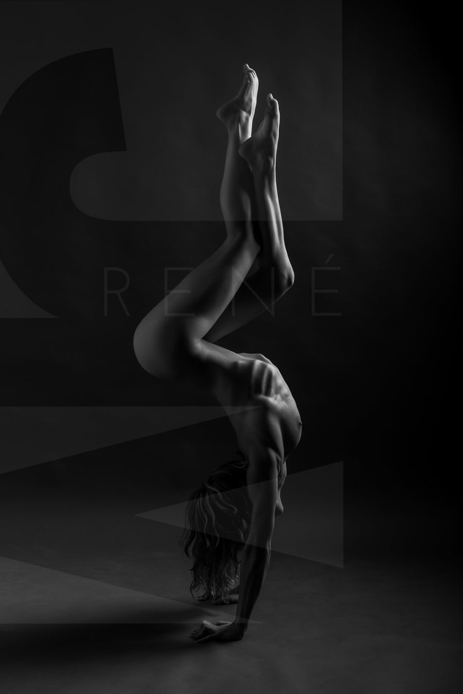 A black and white image showing a side body view of a nude woman in a handstand pose with arched back and crossed bent legs.