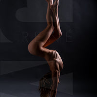 A side body view of a nude woman in a handstand pose with arched back and crossed bent legs.