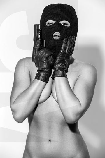 Black and white photo of a nude woman wearing a black balaclava and black gloves holding a handgun, with her hands on her face and the gun resting on the side of her face. 