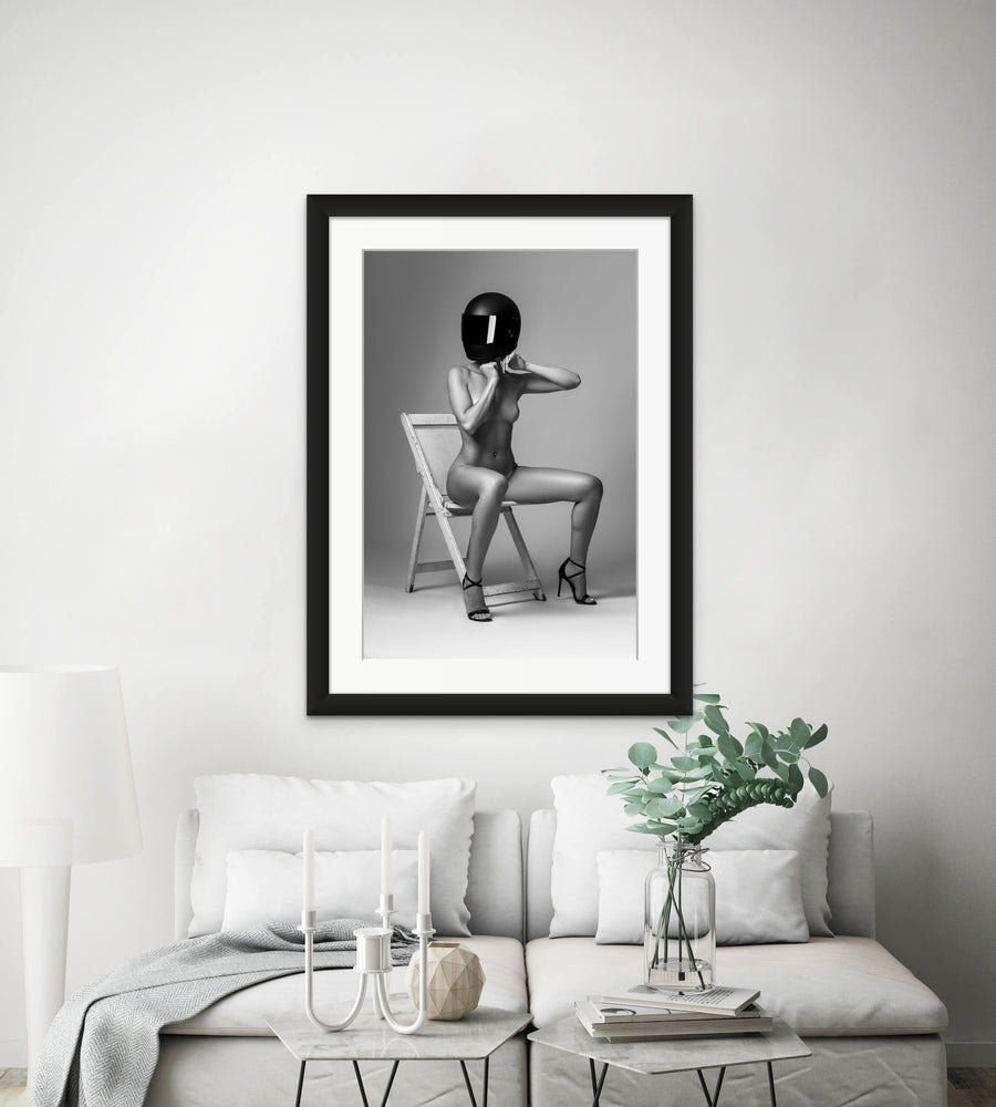 Framed artwork hanging above sofa, the artwork is a black and white photo of nude woman wearing a black motorcyle helmet and black high heels sitting on chair adjusting helmet strap.